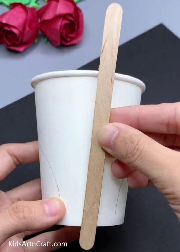 Placing Popsicle Stick On Paper Cup  - Crafting a Swan From Used Paper Cups: A Tutorial For Kids