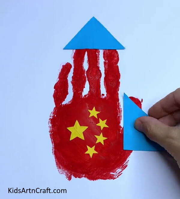 Pasting Blue Triangle On the Thumb - Teach Kids How to Make a Paper Rocket with Handprints.