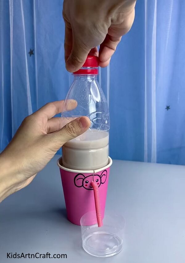 Placing A Cup Under The Straw & Closing The Cap - Putting Together a Reusable Water Fountain with Plastic Bottles and Straws