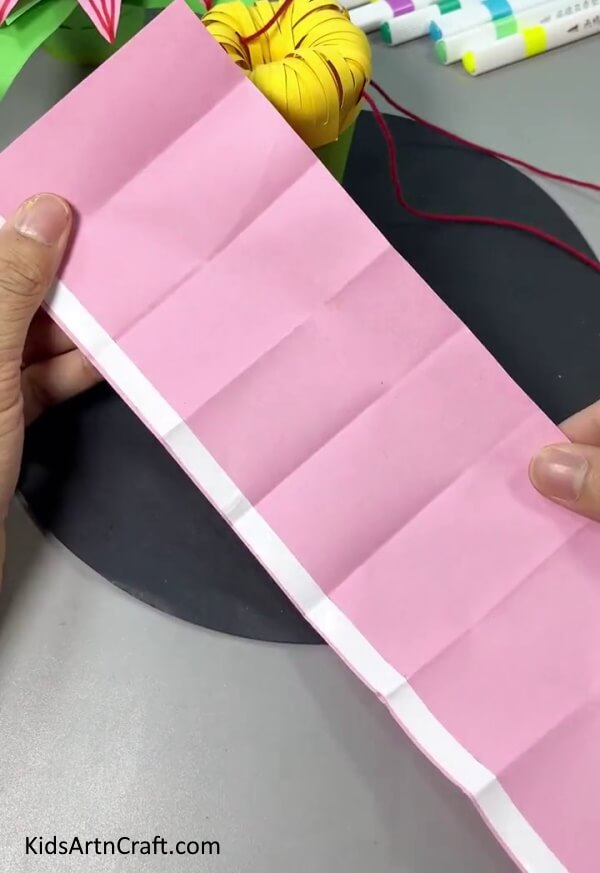 Folding Pink Paper In Equal Parts - Step-by-Step Guide to Making a Paper Flower Hanging