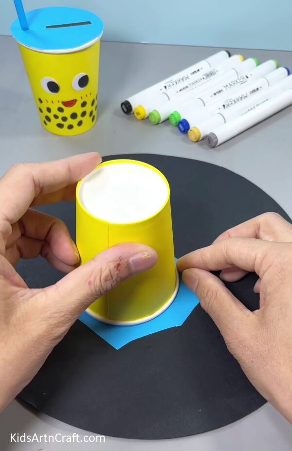 Placing Paper Cup Upside Down On Blue Paper - Design your own recycling craft with this easy-to-do craft.