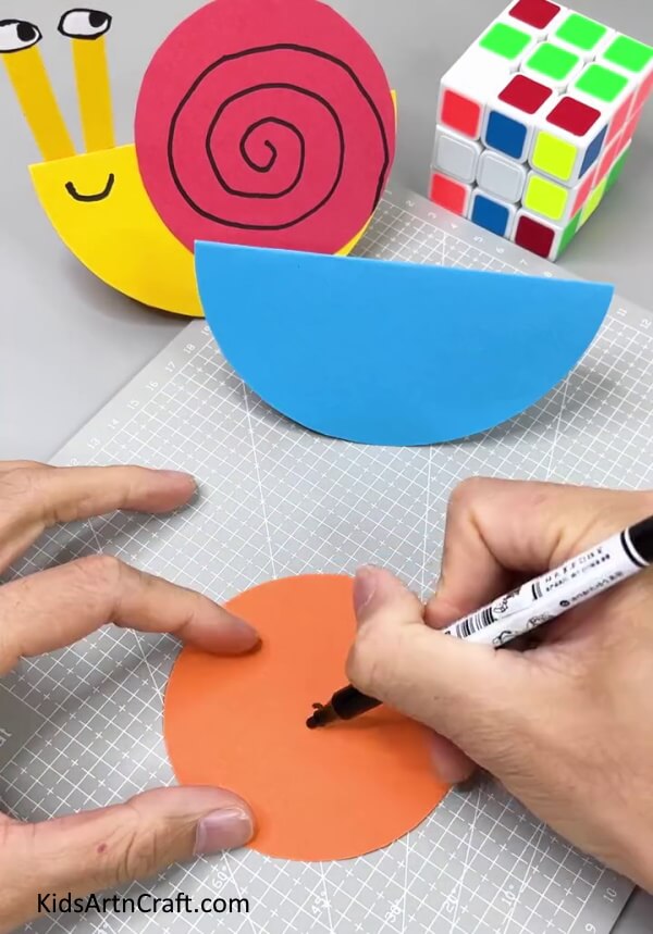Drawing Spiral On Orange Circle - A creative paper snail project that is perfect for kids.