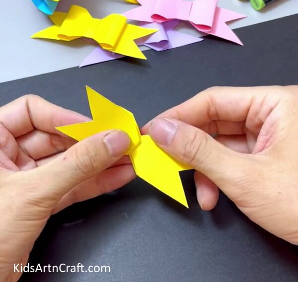 Pushing In Paper To Get Bow Shape - Construct a simple paper bow activity for children.