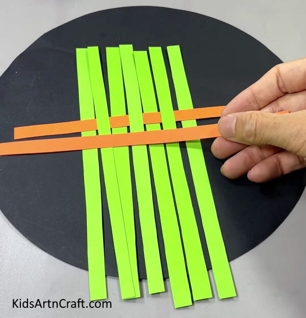 Weaving Orange And Green Strips Together - Learn How to Make a Paper Strip Boat with this Kids Craft Tutorial