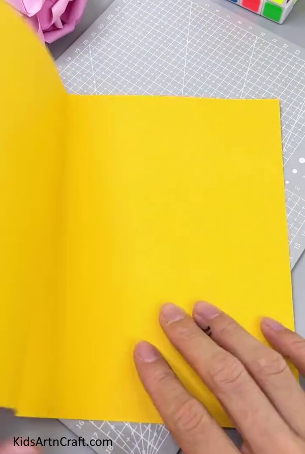 Folding The Yellow Paper In Half - Tutorial for children to create a paper snowman using DIY methods