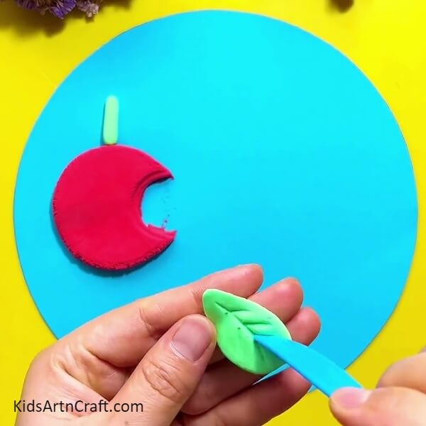 Give shape to the green dough- Artistically Crafting a Caterpillar Eating an Apple Out of Clay 
