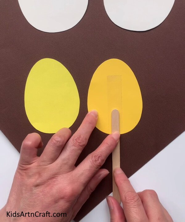 Pasting An Ice Cream Stick A straightforward way to craft Easter Eggs with kids for a colorful look.