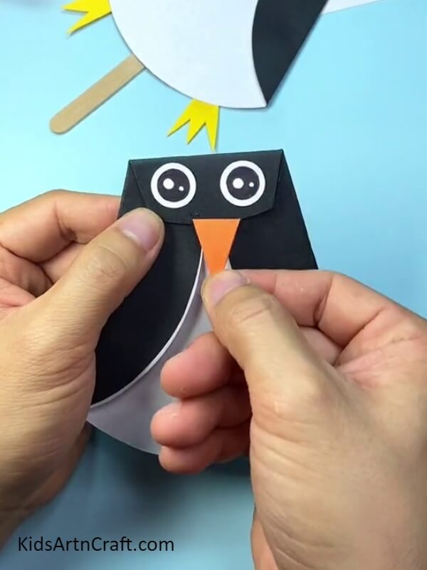 Making the beak of the penguin- Pretty Paper and Popsicle Stick Penguin Creation For Learners