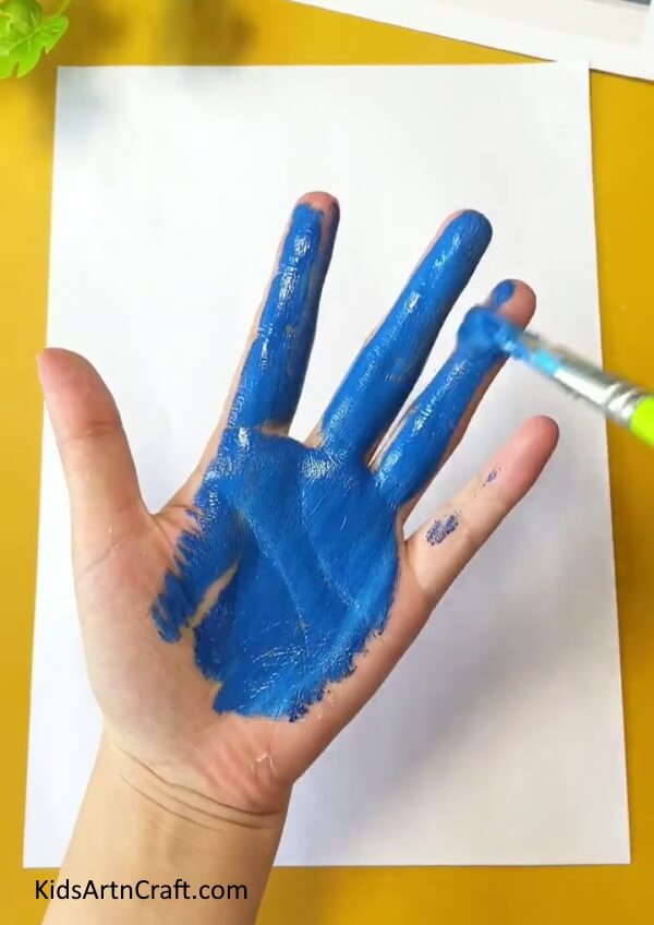 Painting blue color paint on your paw to draw a peacock- An Adorable Peacock Handprint Artwork Project For Children
