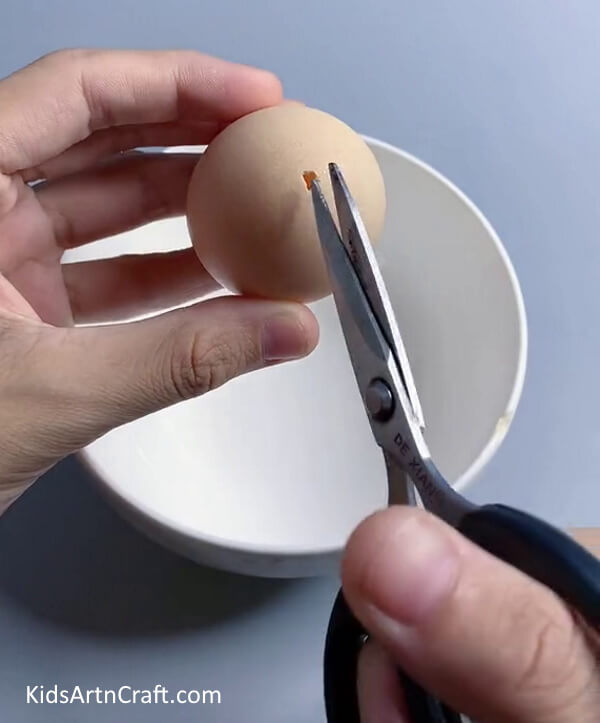 Taking an Egg and Poke a Hole with Scissors- Guide for Crafting an Eggshell Lamp with Children 