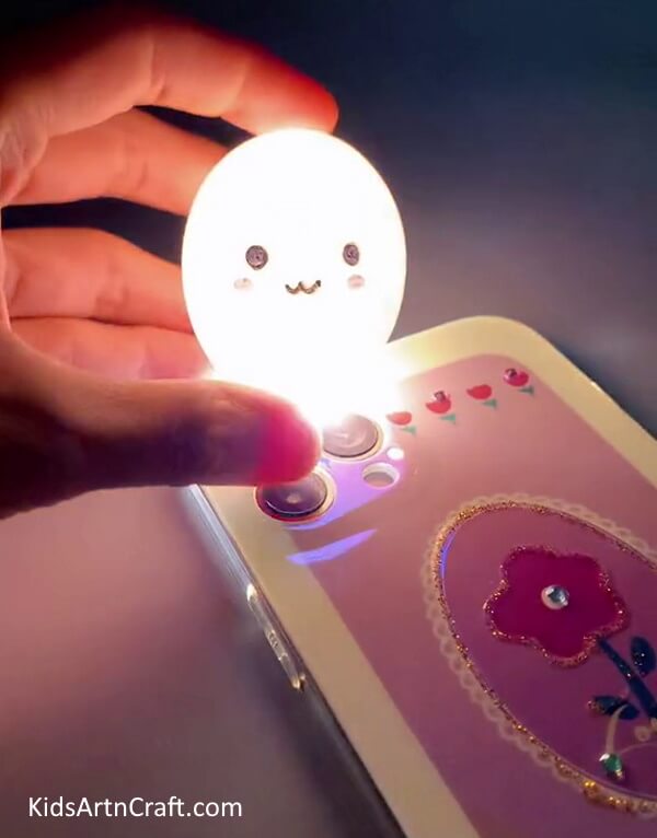 Switching on the flashlight of the mobile phone- Instructions on How to Make a Lamp out of Eggshells with Kids 