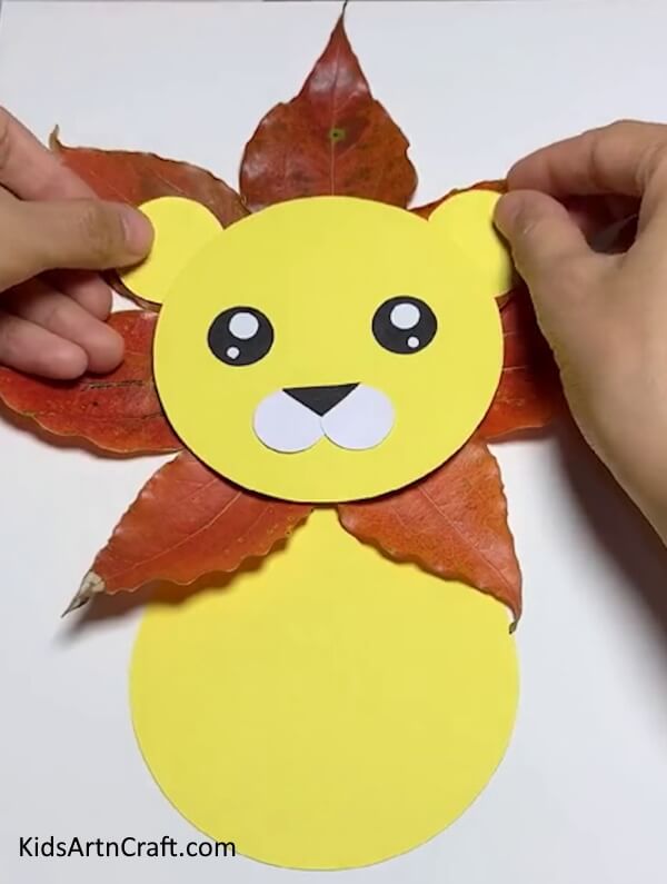 Adding The Ears Of The Lion Using Yellow Craft Paper- A straightforward, kid-friendly method for building a lion out of leaves from fall