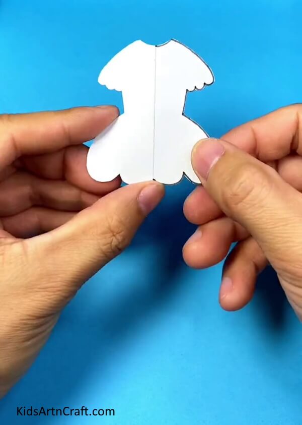 Cutting doll dress from white paper and unfolding it- Kids can have a blast creating their own paper cup costume dolls.