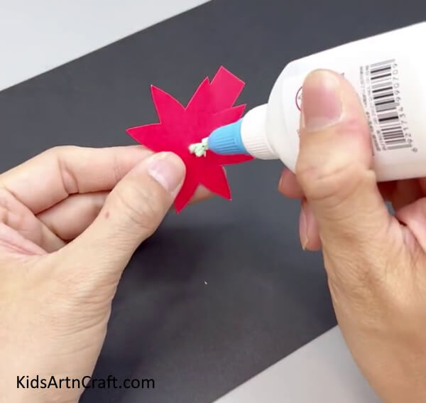 Adding Glue In The Center Of The Red Flower - Teach your kids how to make a Paper Flower Ring using this tutorial 