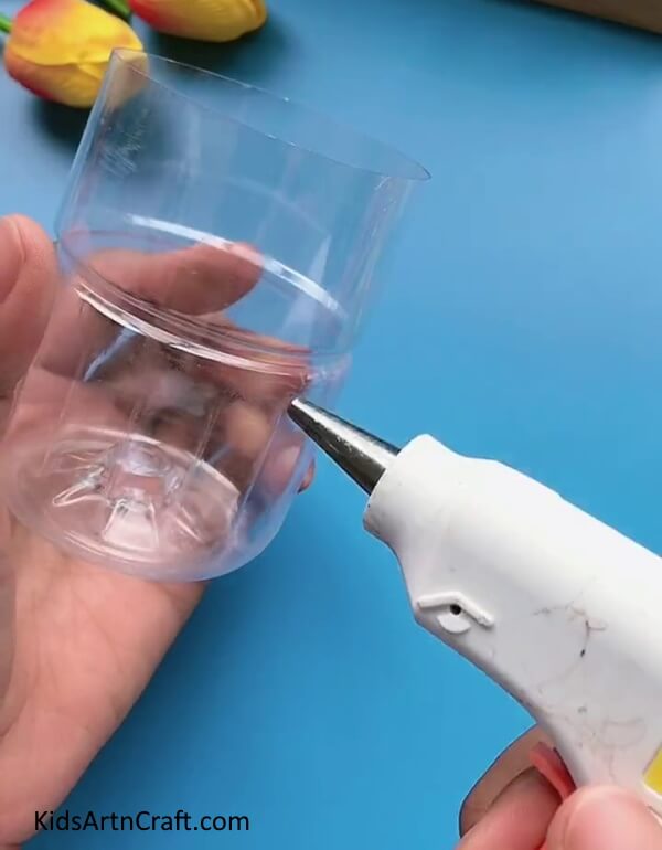 Applying Hot Glue On The Bottle- Make a pencil holder from repurposed plastic containers and colored wire.