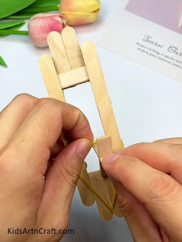 Tying the rubber band on the cross - How To Make Playthings From Popsicle Sticks For Newbies