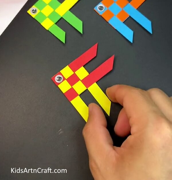 Pasting the single googly eye- A guide for kids to weave a fish out of paper. 