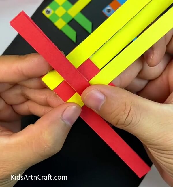 Folding the red strip in the middle- How to construct a paper fish through weaving, for kids. 