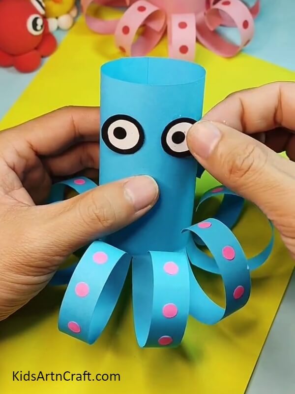 Pasting the eyes on the head- A guide for kids to construct a paper octopus with ease.