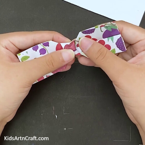 Adjusting the shape in the middle- Step-by-step guide to making a paper bow with origami for children