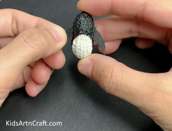 Attaching The Flippers - A grand penguin craft crafted with peanut, thermocol, and a paintbrush.
