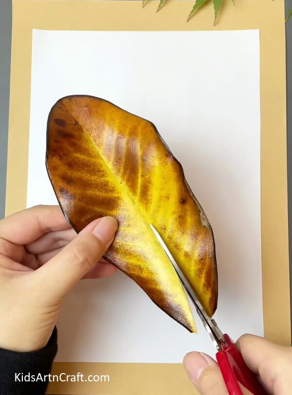 Cutting big fall leaf into two parts- A Simple Tutorial For Creating Autumn Leaves Crafts For Kids