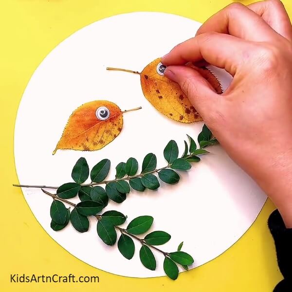 Sticking poppy eyes in the leaves to make birds eyes- Learn to craft a Fall Leaves Bird for kids - a DIY tutorial.