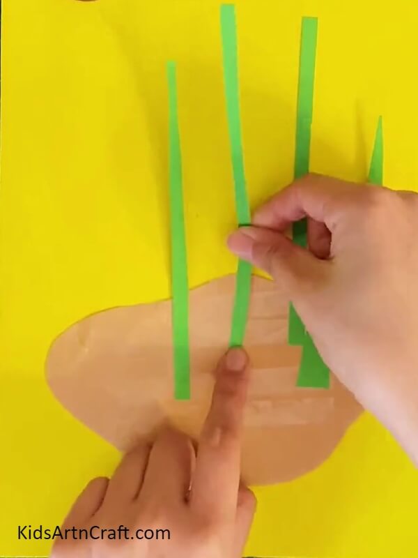 Pasting Thin Green Strips On Brown Color Craft Paper-Constructing a Lily Paper Flower Art For Children