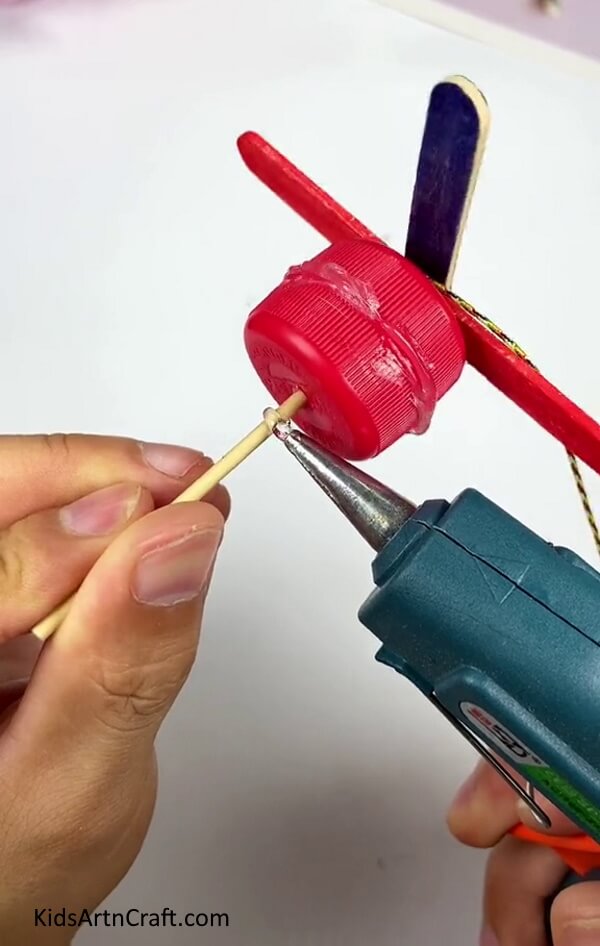 Applying Glue To The Toothpick - Fabricating a Pinwheel with the help of Popsicle Sticks and a bottle cap
