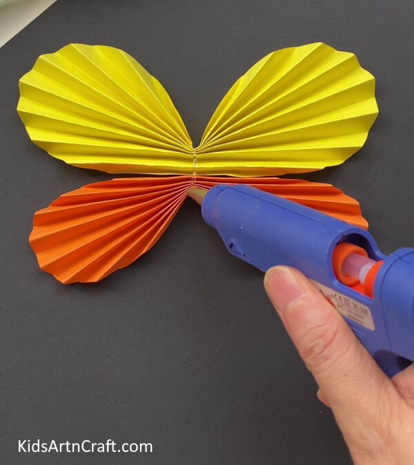 Sticking The Ice Cream Stick Over The Wings - Guide to Creating a Paper Butterfly with Kids