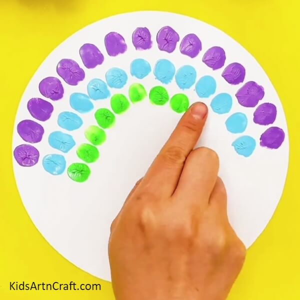 Dip your index finger in green paint and make similar impressions but reduce the size of the pattern- Stylish Peacock Fingerprint Art Idea For Kids