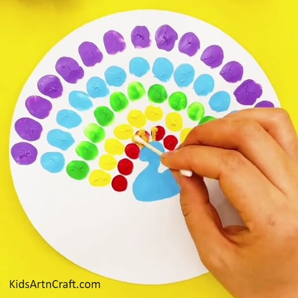Take a cotton bud, dip it in yellow paint and draw the crest of the peacock above its head- Fun Fingerprint Artwork Of A Peacock For Kids