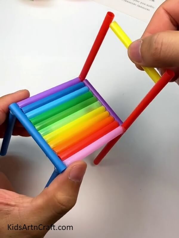 Pasting piece of yellow straw with top of red straws- How to Make a Rainbow Straw Chair Tutorial for Inexperienced 