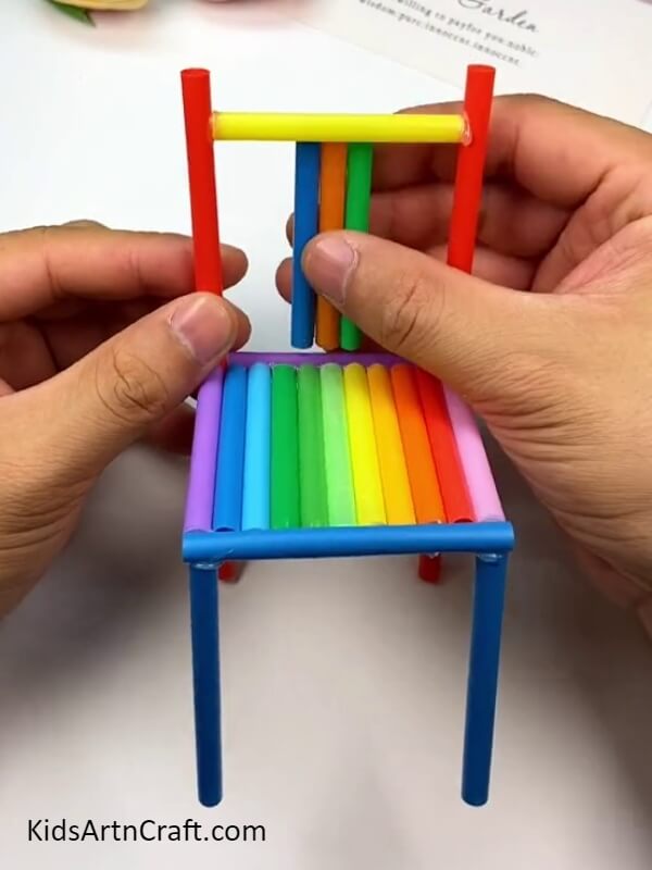 Cutting small pieces from blue, orange and green straw and pasting it- Tutorial for Designing a Rainbow Straw Chair for Novices 