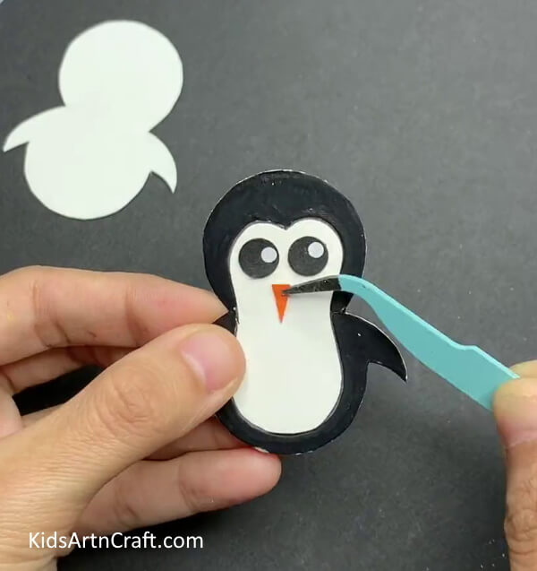 Cutting Out The Eyes And Nose And Paste Them- Crafting a Rocking Paper Penguin Toy Employing Bottle Cap and Clay