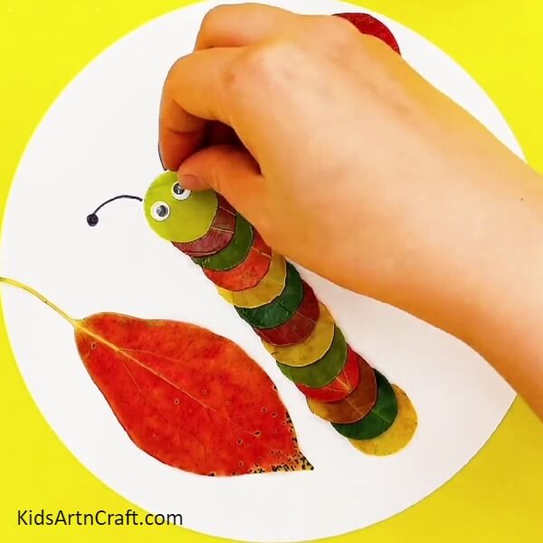 Making Eyes And Antennas Of The Caterpillar-Children having fun making a charming caterpillar out of autumn leaves