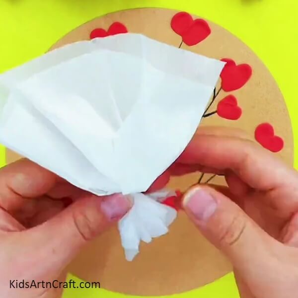 Tying the tissue paper at the bottom- An art and craft endeavor for kids involving heart-shaped elements, clay, and paper