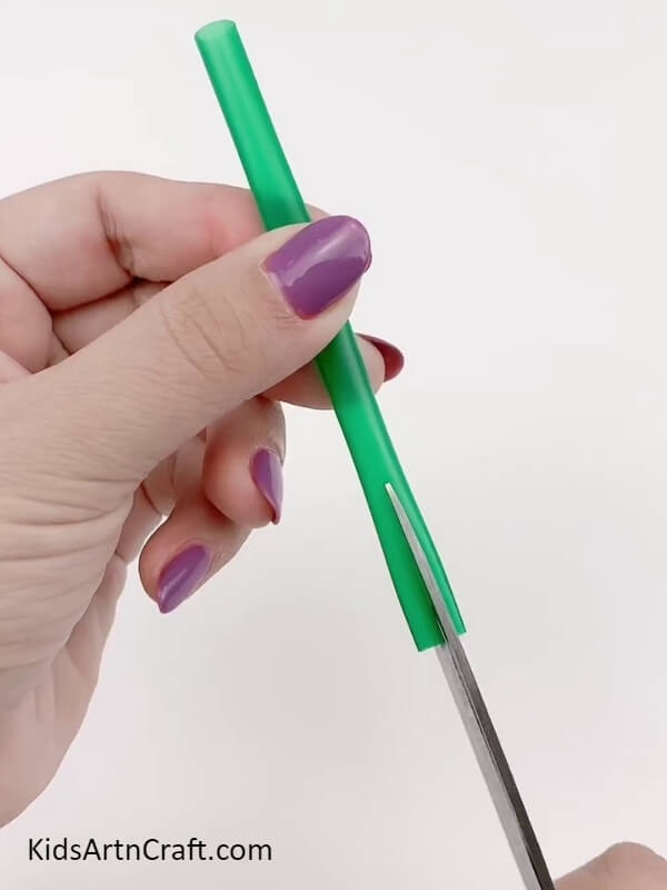 Cutting a green straw into half- Step-by-step tutorial to create a plastic straw falling flower craft for Kids