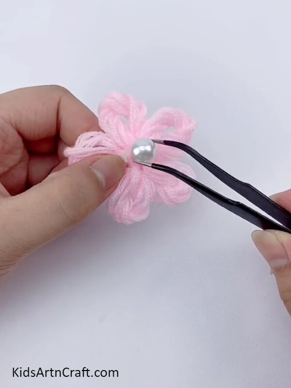 Stick the pearl in the middle of the pink wool flower- An easy-to-follow tutorial to making an attractive flower wreath with cardboard and wool for little ones. 