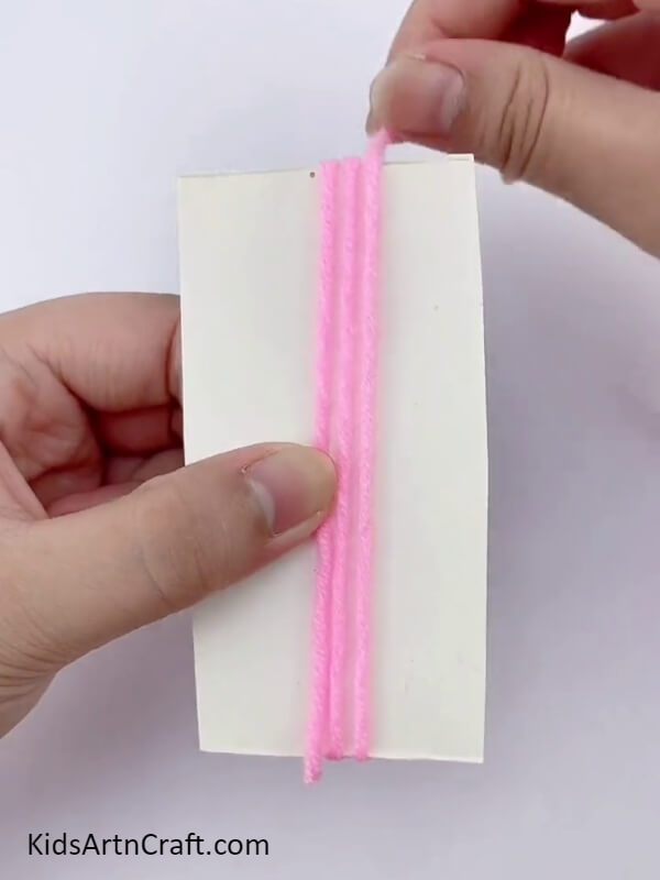 Wrap the dark pink wool around rectangular cardboard- A how-to for creating a lovely flower wreath with cardboard and wool for children. 