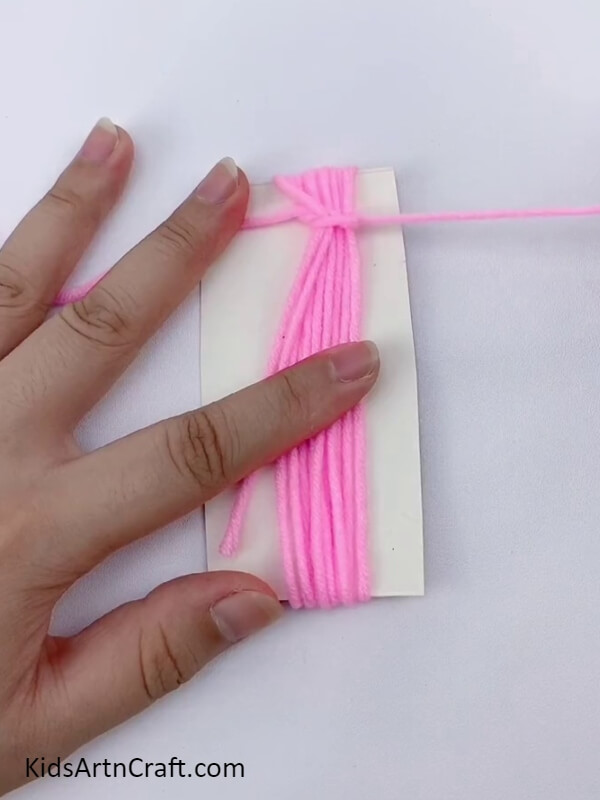 Tie a knot from the dark pink wool- Directions for assembling a gorgeous flower wreath with cardboard and wool for kids. 