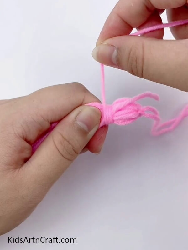 Tie the dark pink wool to make a tassel- A tutorial for children on producing an appealing flower wreath with cardboard and wool.