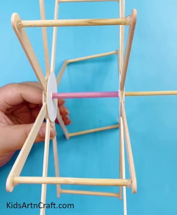 Inserting A Straw And Stick In The Holes Of Circles-Make a Fun Ferris Wheel with Recycled Sticks and Bottle Caps for the Children.