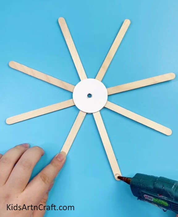 Applying Glue To The End Of Popsicle Stick-An Artistic Project for the Kids: A Ferris Wheel Using Reused Sticks and Bottle Caps