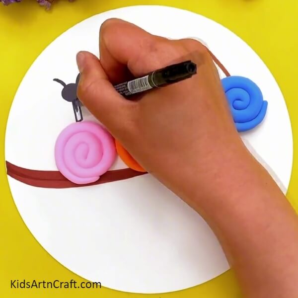 Making The Snail's Body- A clay-paper craft made by kids that includes snails on a tree branch. 