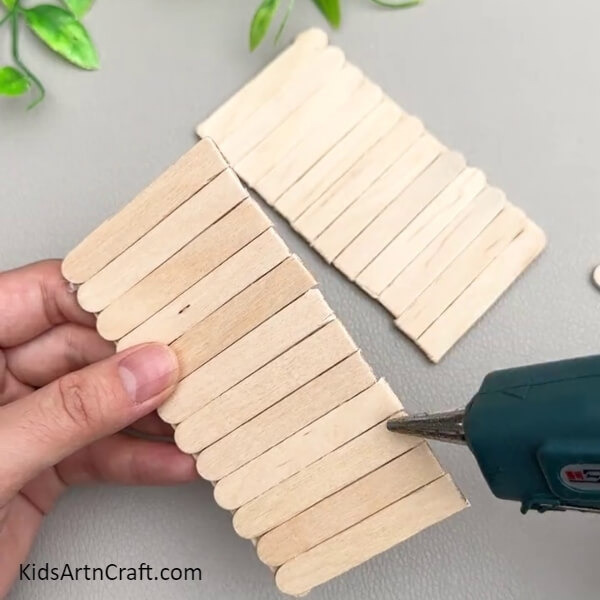 Applying Hot Glue On The Back-Enchanting Swing Craft Using Popsicle Sticks For Toddlers