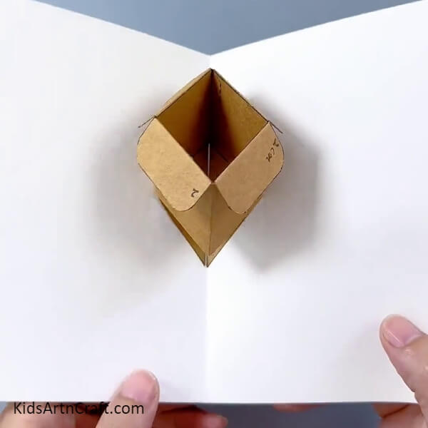 Pasting The Other Triangle To The Paper- Learn how to make a flower pot from a cardboard box with this instructional for kids