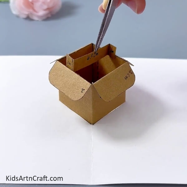 Inserting A Cardboard Strip- An activity guide on how to craft a flower pot from a cardboard box for children.