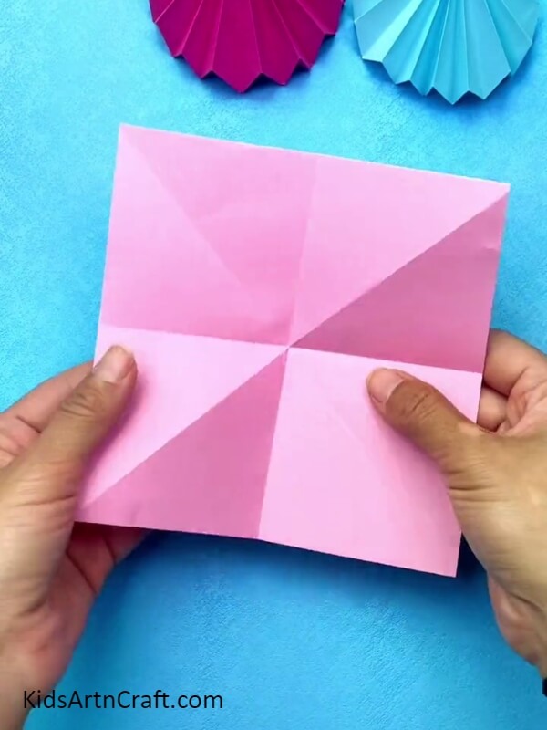 Making Creases On A Pink Origami Paper- How to Make an Origami Ball Gown for Children