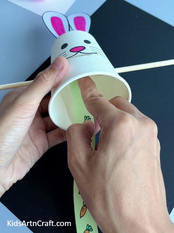 Sticking The Strip To The Wooden Stick- A paper cup bunny munching on a carrot is an enjoyable activity for kids.